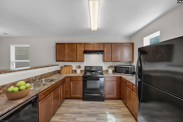 kitchen with black appliances, under cabinet range hood, brown cabinetry, and a sink