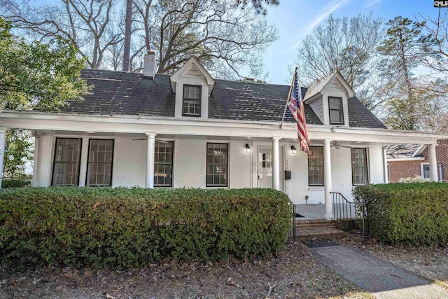 cape cod house with ceiling fan, a chimney, a porch, and brick siding