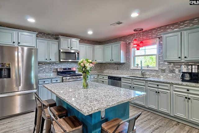 kitchen featuring stainless steel appliances, visible vents, a sink, light wood-type flooring, and a kitchen bar