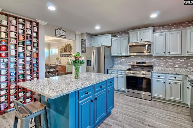 kitchen featuring blue cabinets, stainless steel appliances, backsplash, light stone countertops, and light wood finished floors