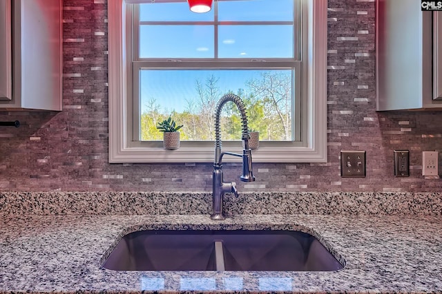 kitchen with a healthy amount of sunlight, tasteful backsplash, dark stone counters, and a sink