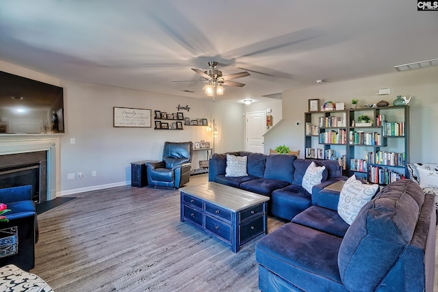 living room featuring visible vents, a ceiling fan, a glass covered fireplace, wood finished floors, and baseboards