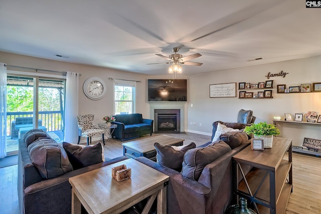 living area featuring baseboards, a glass covered fireplace, visible vents, and light wood-style floors