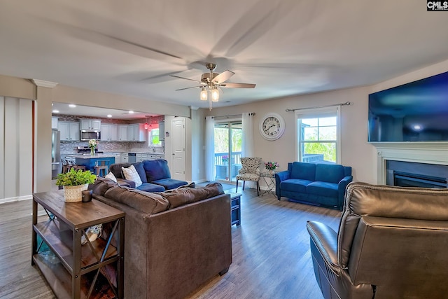 living room featuring a ceiling fan, a fireplace, baseboards, and wood finished floors