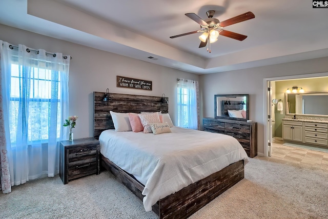 bedroom with a raised ceiling, light carpet, baseboards, and ensuite bathroom