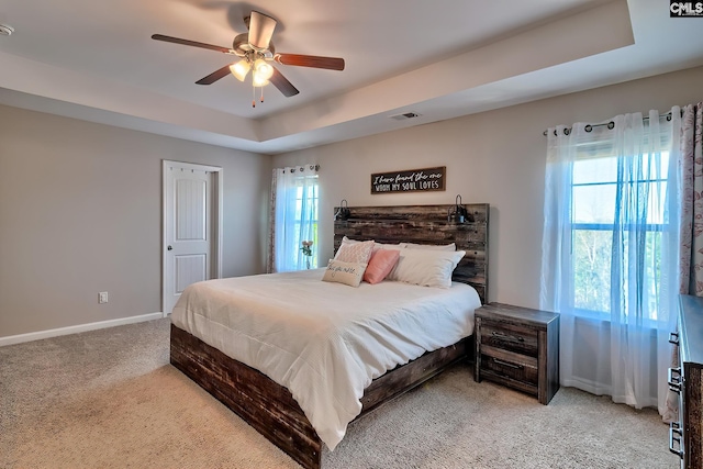 carpeted bedroom featuring visible vents, a tray ceiling, ceiling fan, and baseboards