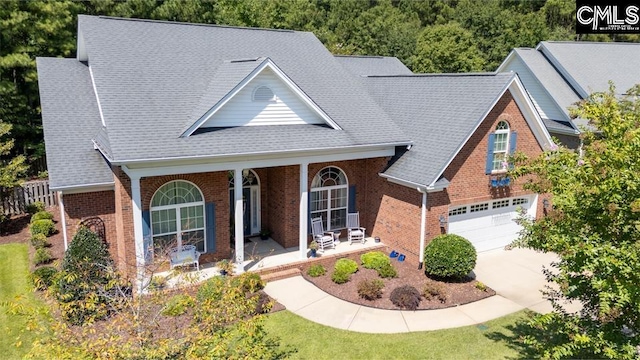 view of front facade featuring a garage, a shingled roof, concrete driveway, covered porch, and brick siding