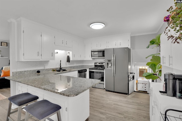 kitchen featuring light stone counters, a peninsula, a sink, appliances with stainless steel finishes, and crown molding