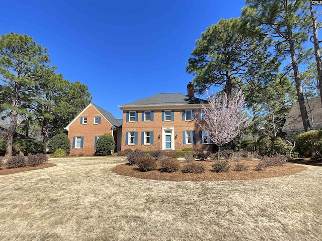 colonial inspired home with a chimney and brick siding