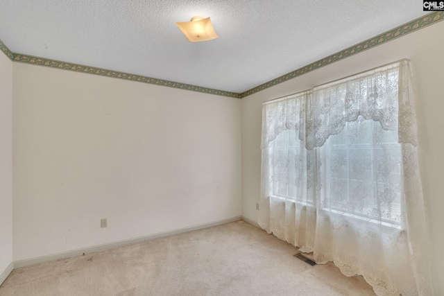 spare room featuring light carpet, visible vents, baseboards, and a textured ceiling