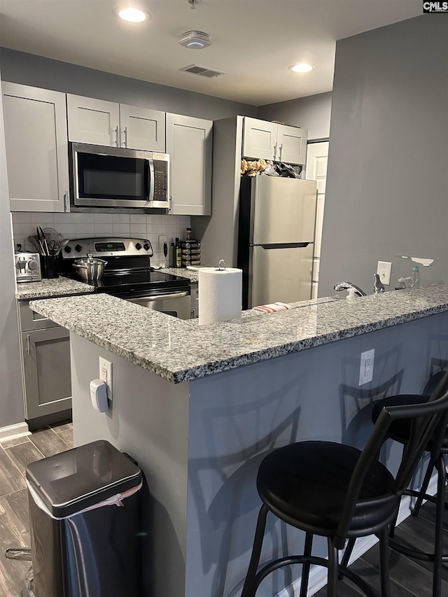 kitchen with a breakfast bar area, tasteful backsplash, visible vents, appliances with stainless steel finishes, and light stone countertops