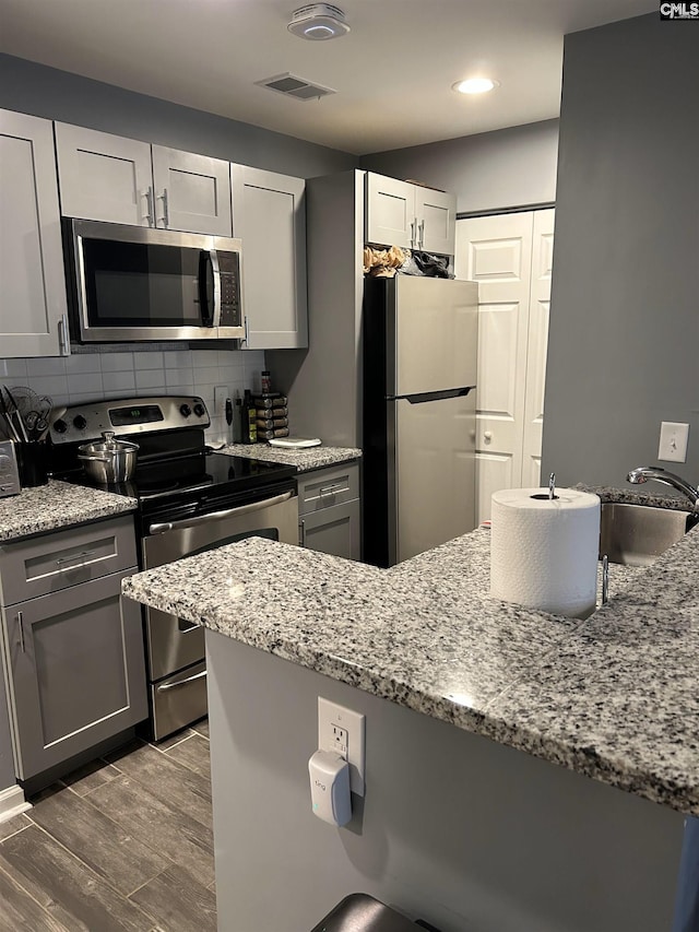 kitchen featuring visible vents, decorative backsplash, light stone counters, wood tiled floor, and stainless steel appliances