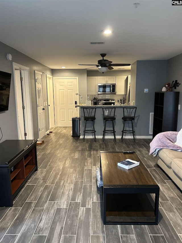 living room featuring wood tiled floor, visible vents, ceiling fan, and baseboards