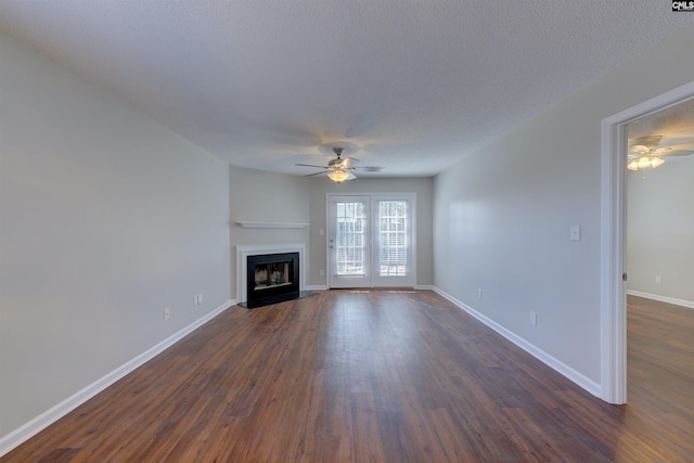 unfurnished living room featuring a fireplace with flush hearth, dark wood-type flooring, baseboards, and a ceiling fan