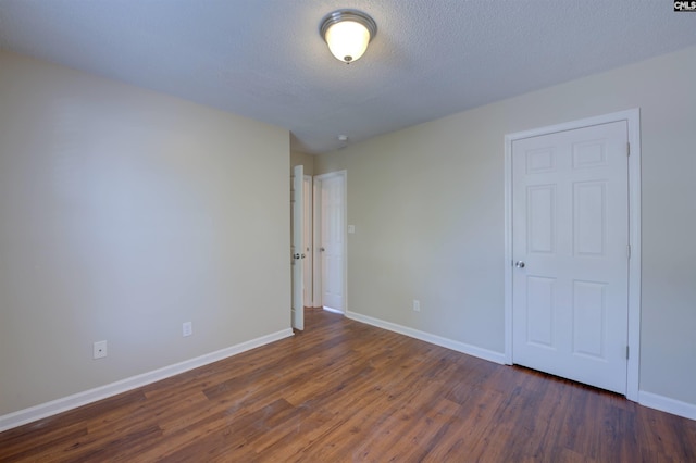 unfurnished room featuring a textured ceiling, dark wood finished floors, and baseboards