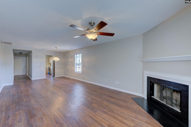 unfurnished living room featuring dark wood-type flooring, visible vents, a fireplace, and a ceiling fan