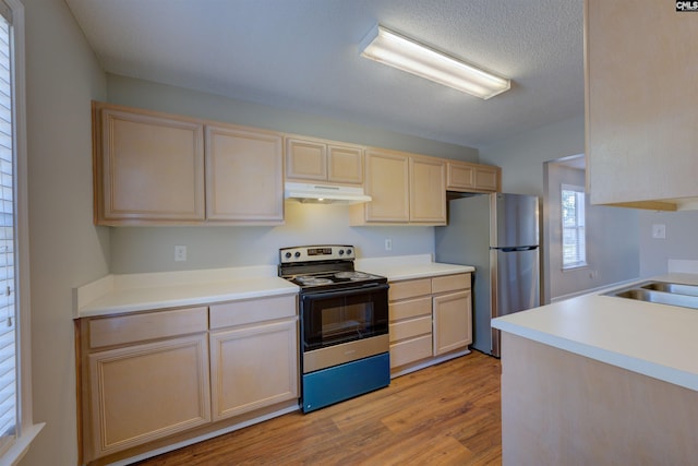 kitchen featuring electric range, light brown cabinetry, freestanding refrigerator, a sink, and under cabinet range hood