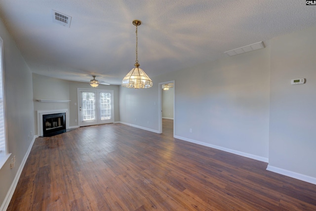 unfurnished living room with dark wood-type flooring, baseboards, visible vents, and a fireplace with flush hearth