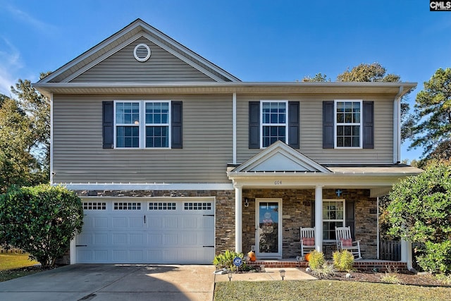 view of front of house featuring driveway, stone siding, an attached garage, covered porch, and a standing seam roof