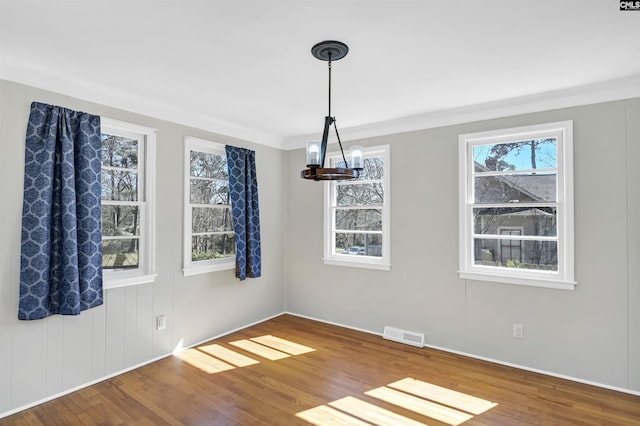 unfurnished dining area featuring a chandelier, visible vents, crown molding, and wood finished floors