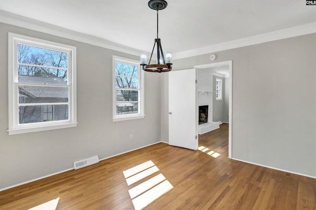 unfurnished dining area with ornamental molding, visible vents, a fireplace, and wood finished floors