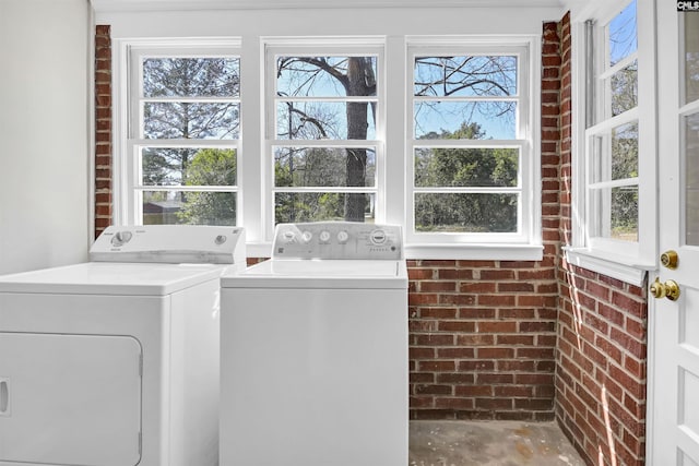 clothes washing area with laundry area, washer and clothes dryer, and brick wall