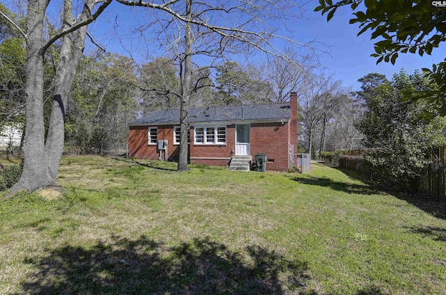 back of house with entry steps, brick siding, a yard, and a chimney