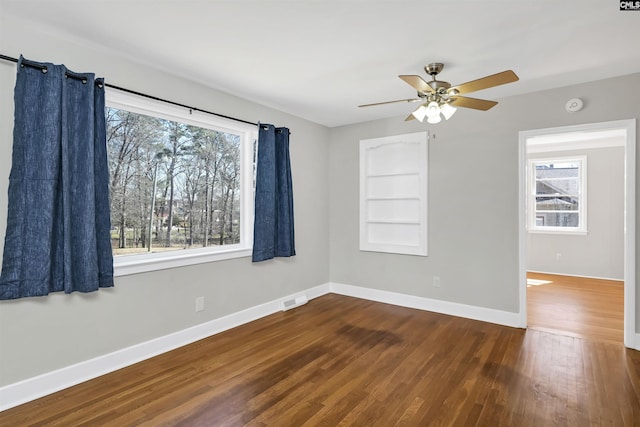 empty room featuring baseboards, visible vents, ceiling fan, and dark wood-style flooring