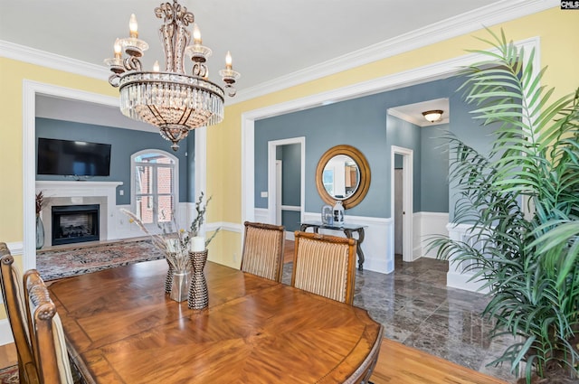 dining area featuring an inviting chandelier, wainscoting, ornamental molding, and a high end fireplace