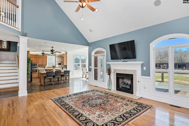 living room featuring light wood-style flooring, a fireplace, stairway, and ornate columns