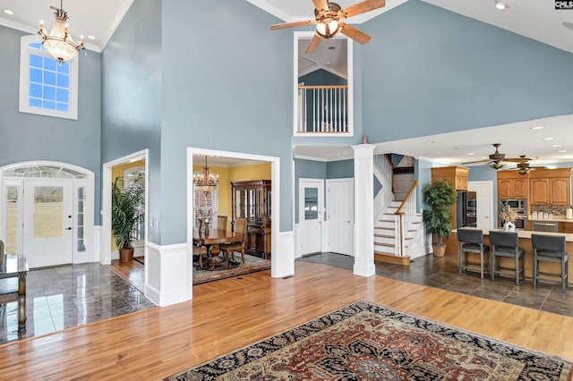 foyer with ceiling fan with notable chandelier, stairway, crown molding, and wood finished floors