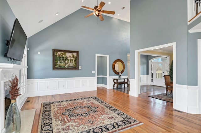 living room featuring a premium fireplace, wood finished floors, visible vents, a ceiling fan, and wainscoting