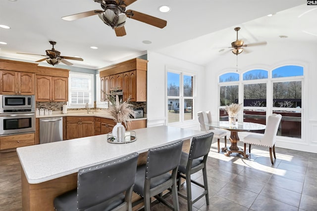 kitchen featuring light countertops, appliances with stainless steel finishes, decorative backsplash, and brown cabinets