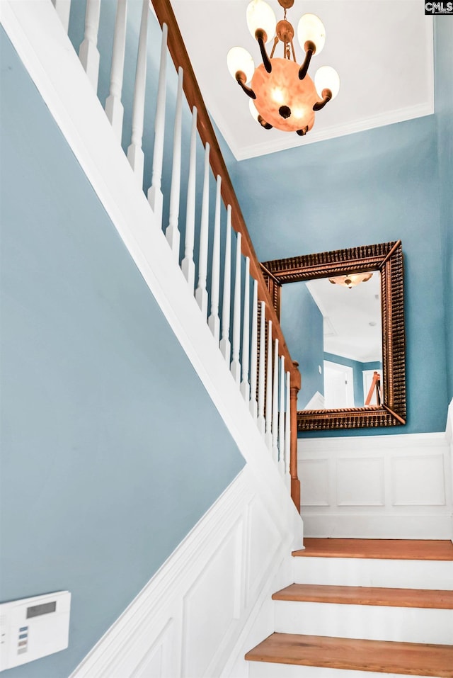 stairway with crown molding, a decorative wall, wainscoting, and an inviting chandelier