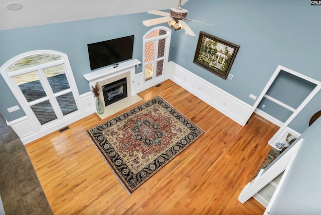 living area with lofted ceiling, visible vents, a fireplace with flush hearth, a ceiling fan, and wood finished floors