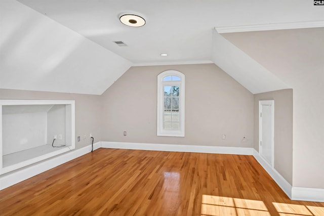 additional living space featuring light wood finished floors, baseboards, visible vents, and vaulted ceiling