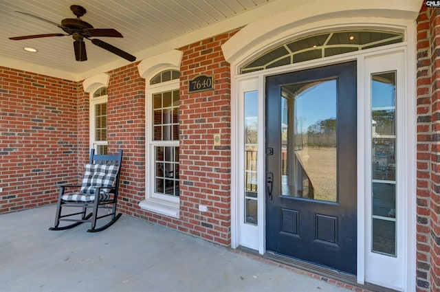 view of exterior entry featuring a porch, a ceiling fan, and brick siding