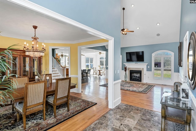 dining area featuring ceiling fan with notable chandelier, a wainscoted wall, crown molding, and wood finished floors