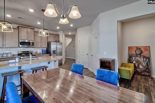 kitchen featuring visible vents, appliances with stainless steel finishes, dark wood-type flooring, a kitchen bar, and backsplash