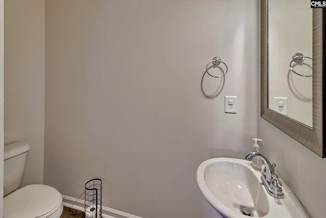 half bath featuring baseboards, a sink, and toilet