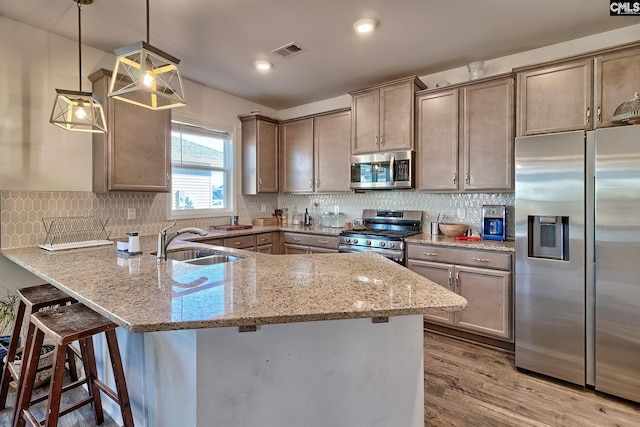 kitchen with a peninsula, a sink, visible vents, appliances with stainless steel finishes, and light stone countertops