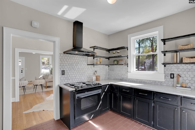 kitchen with tasteful backsplash, wall chimney exhaust hood, black stove, and open shelves