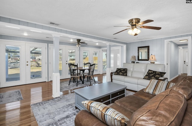 living area with french doors, wood finished floors, visible vents, and ornate columns