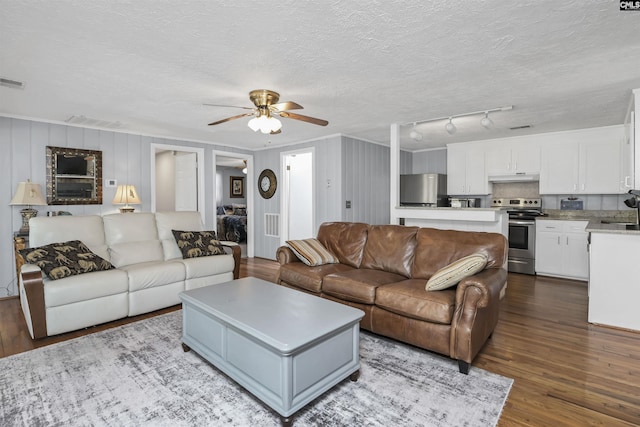 living area featuring a textured ceiling, dark wood finished floors, visible vents, and a ceiling fan