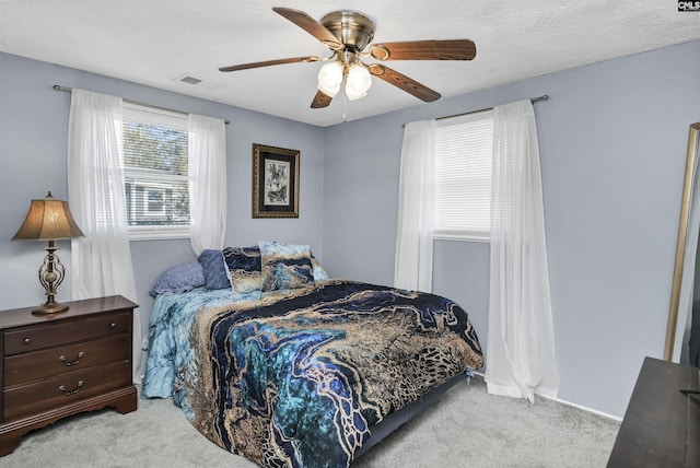 carpeted bedroom featuring ceiling fan, a textured ceiling, visible vents, and baseboards