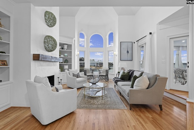 living area with built in features, a fireplace, a high ceiling, and wood finished floors