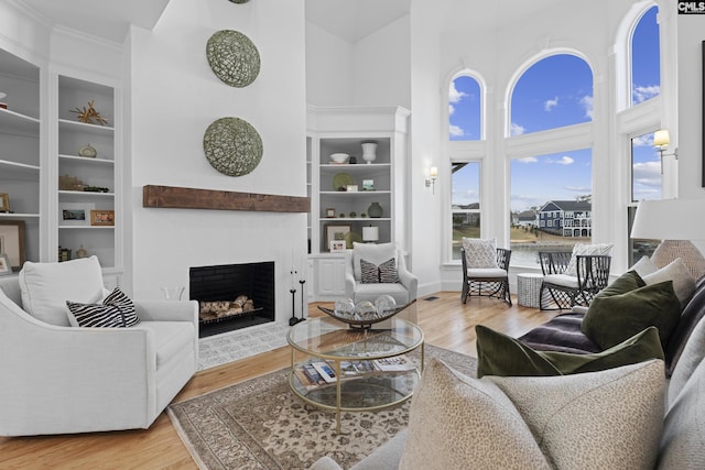 living area with built in features, a fireplace with flush hearth, wood finished floors, and a towering ceiling