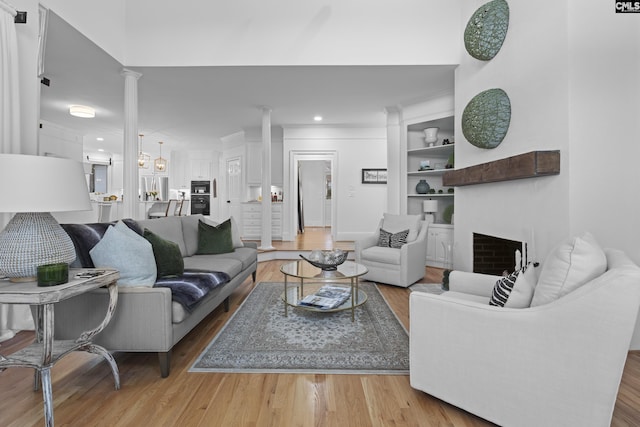 living area featuring built in features, a fireplace, light wood-style floors, and ornate columns