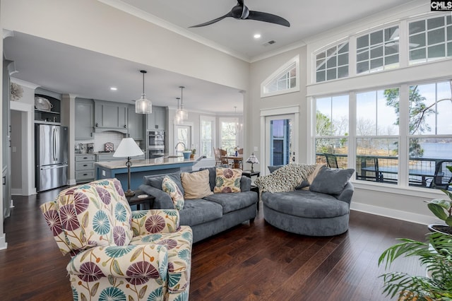 living area with a ceiling fan, visible vents, baseboards, ornamental molding, and dark wood finished floors