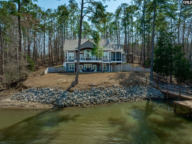 rear view of house featuring driveway, a sunroom, and a deck with water view